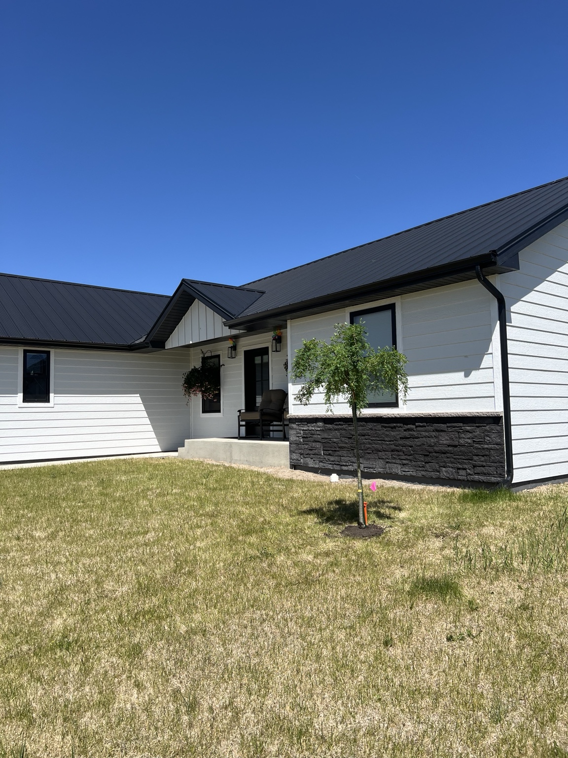 Finished Montana custom home with white siding, stone accents, and black metal roof